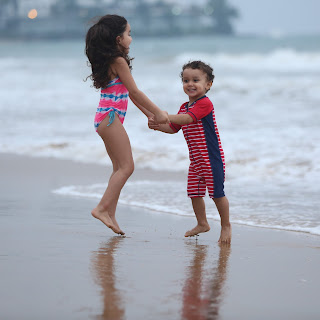 Girl and boy holding hands and jumping in water at beach