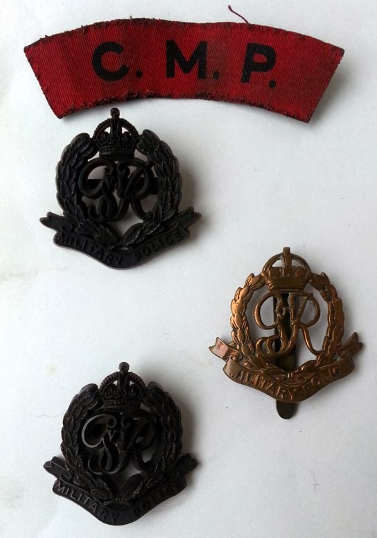 A red cloth shoulder flash with letter C.M.P. and two brown plastic badges and a brass badge all with GVIR in the centre of a wreath, crown above, Military Police in a scroll below