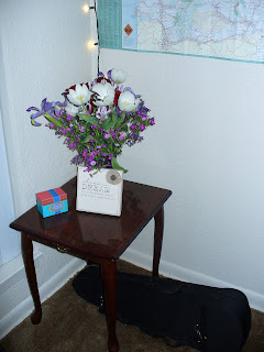 A vase of flowers on a small end table with a violin case underneath it.