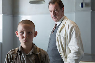 A young boy with shaved head Ernst Lossa (Ivo Pietzcker)  is being viewed by a doctor Dr. Werner Veithausen (Sebastian Koch) standing behind him. Courtesy of StudioCanal.