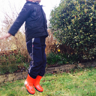 Boy in red wellington boots jumping in a park with a grey sky over head - Tip five tips for helping autistic kids in wet weather
