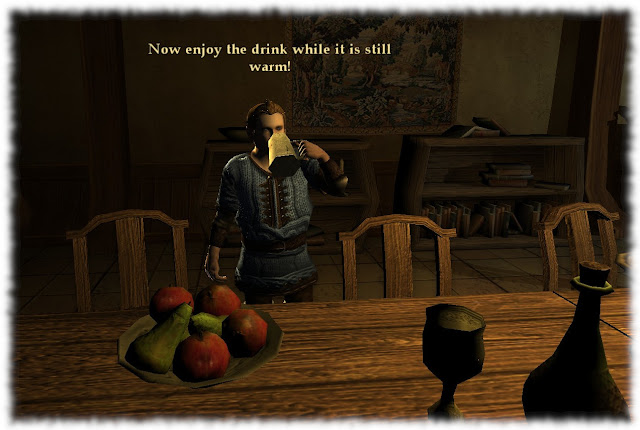 Gifio is standing by a table indoors. There is a plate of apples, a goblet and a bottle. Gifio is drinking from a mug. "Now enjoy the drink while it's still warm!"