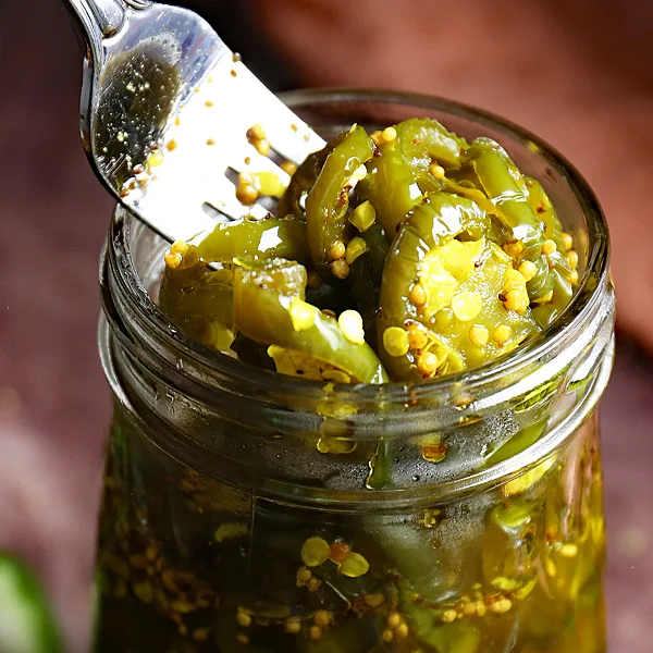 Close-up of Cowboy Candy in a Jar: A fork delicately picks up spicy jalapenos, revealing the mouthwatering heat and sweet flavors of homemade cowboy candy