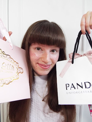 Smiling whilst holding up two pretty shopping bags. One Pandora and one Miss Ellie