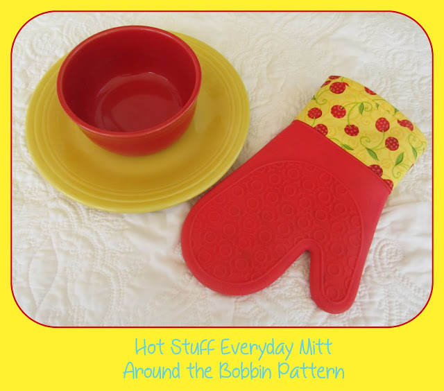 Red bowl, yellow plate underneath with an oven mitt in red silicone with a fabric cuff of red cherries and yellow background fabric