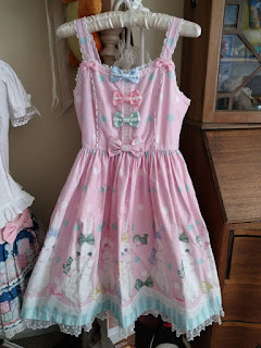 Sweet lolita JSK featuring bunnies wearing bows of different colours and birds.. The bottom of the dress has a striped boarder with lace. The bodice has three satin bows in different colours down the front and at the bottom a bow that's the same material as the dress. The shoulder straps also have small bows on them. The dress has polkadots.
