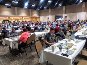 The main convention hall. A large area filled with tables, with most of the seats taken by people playing board games.