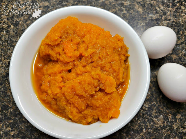 A white bowl of pumpkin puree, next to two eggs.