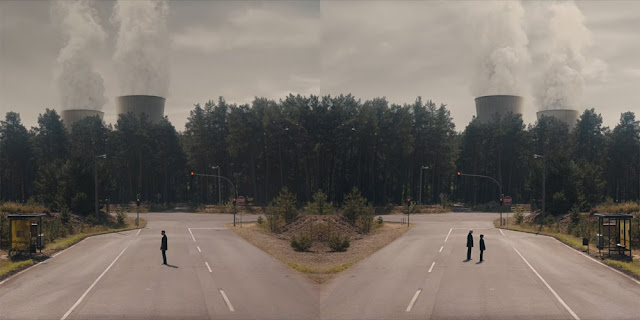 In two parallel worlds, men stand in front of a nuclear power plant