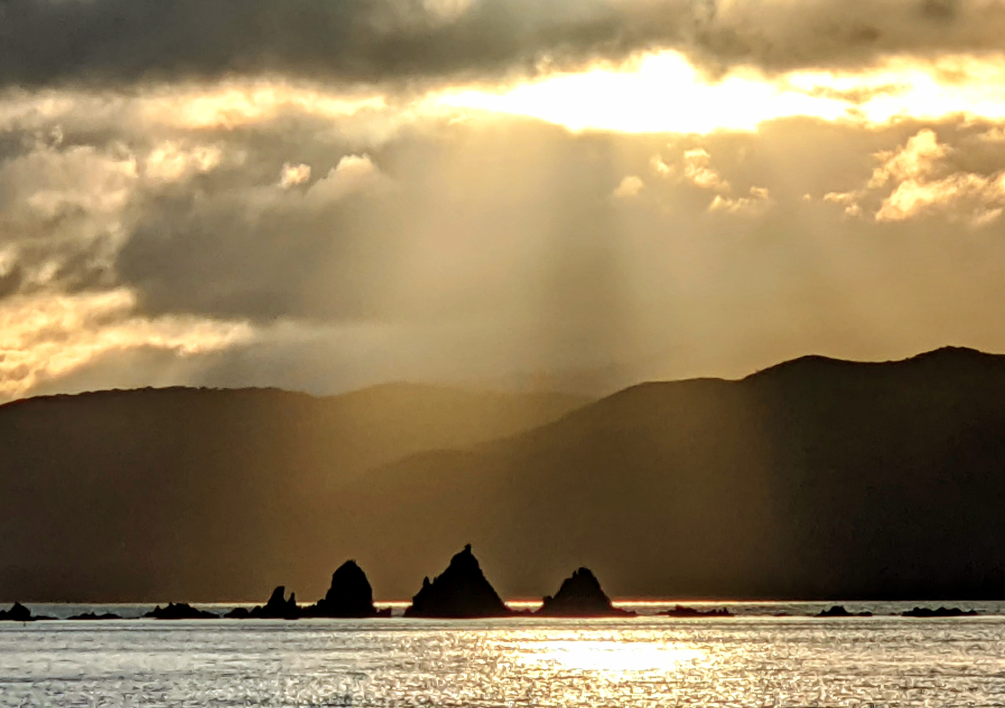 Honey coloured sunrise casts rays over 3 pointy rocks in Breaker Bay