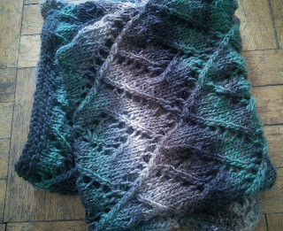 A folded lace scarf, knit with worsted-weight colour changing yarn  Colour changes from beige; grey; brown; black; and forest green. 