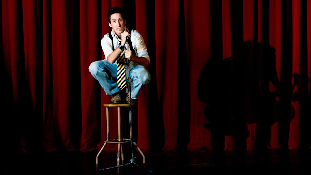 comedian sitting on stool