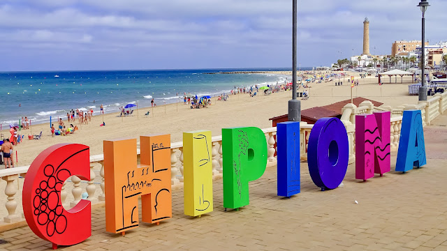 Cartel de Chipiona en el paseo marítimo con letras de colores y la playa y el mar de fondo.