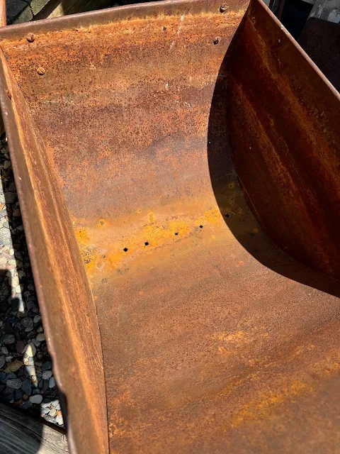 Photo of holes made in the bottom of a rusty garden cart.