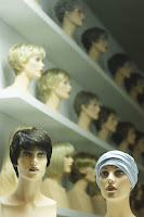 Photo of numerous mannequin heads on shelves with different wigs on, some blonde some brunette