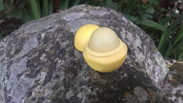 A Lemon drop EOS lip balm open and on a rock with the lid next to it