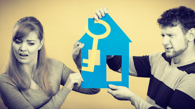 A couple holding a cut-out of a house. They appear apprehensive about moving in together. 