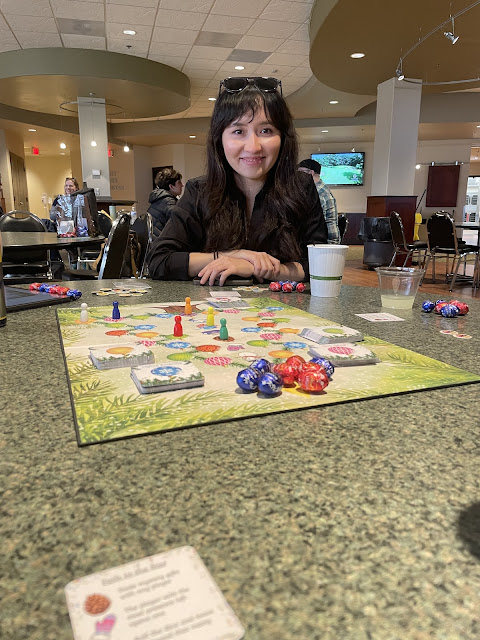 woman smiling at the camera with the game board mid-play on the table in front of her