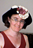 Cynthia Parkhill wearing black hat with the brim folded up in front and a large pink and white flower attached to it.