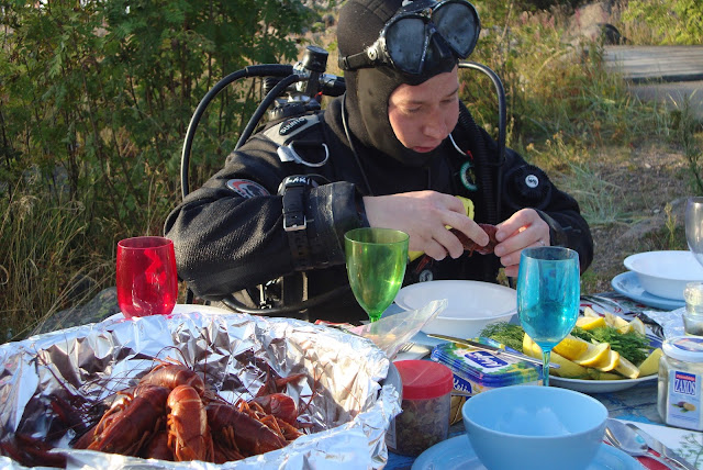 Sukelluspukuinen henkilö istuu ruokapöydässä, jossa on tarjolla rapuja