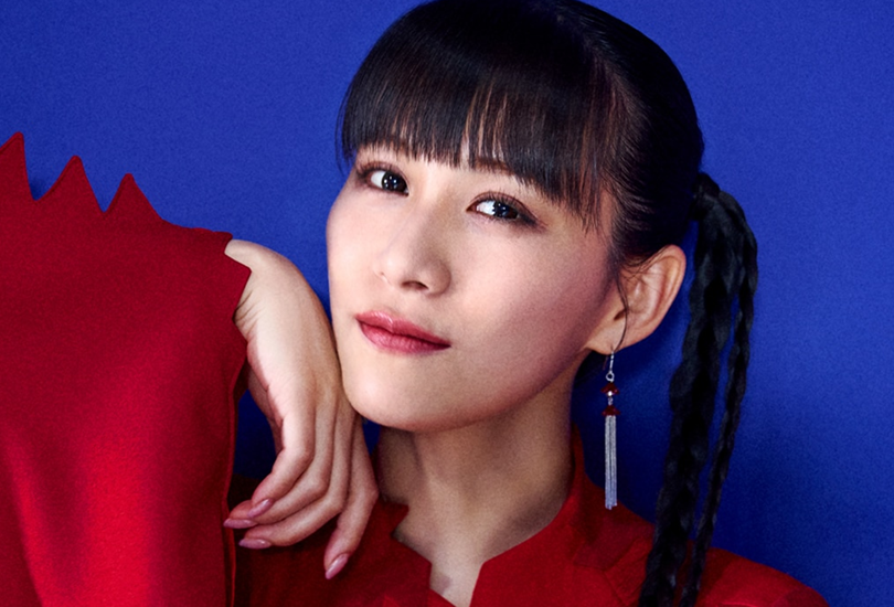 a-chan of Perfume, posing against a blue backdrop, wearing a red dress.