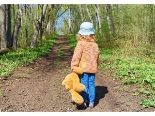 A girl walking on a trail in the woods carrying her teddy with her