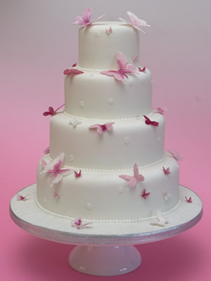 White iced wedding cake over four round tiers decorated with pink 