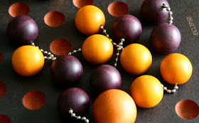 A close up of the pieces on the board in the middle of a game. You can see several vacant holes, but most of them are occupied by the little pairs of wooden balls linked by dog-tag style chains. Some of these pairs are a light orangish-brown colour; the others are a dark purpley-brown. A couple of the pairs are arranged so that their chains cross over the chain of another pair. In the bottom of the picture, one of the light coloured balls is larger than all the others, and is not linked to another.