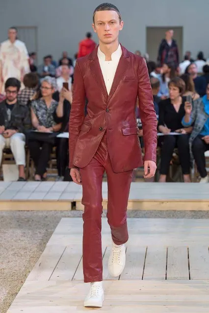 A serious faced fashion model wearing a red leather suit walking down the runway