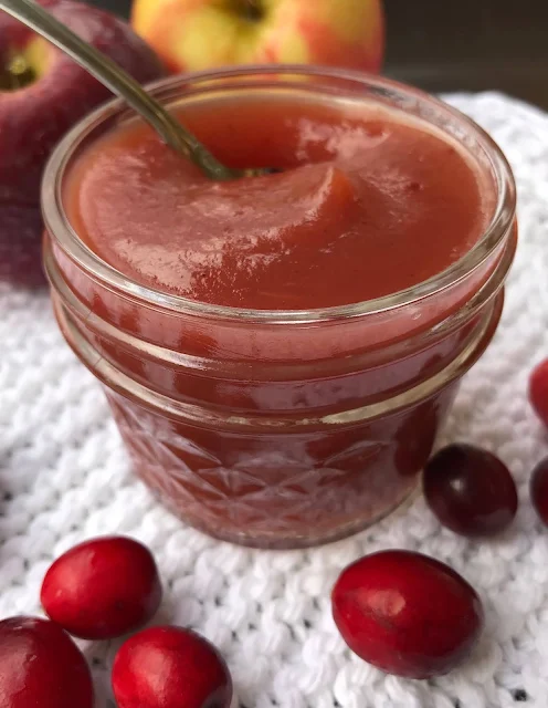 Side view of a finished jar of cranberry apple butter with a spoon inside.