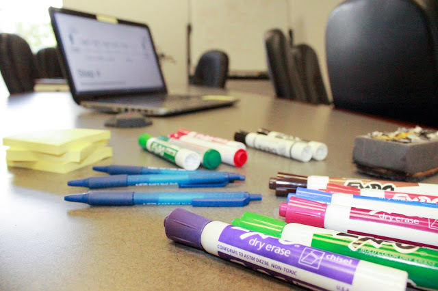 Dry erase markers, whiteboard eraser pens, post it note pads, and a laptop on a table