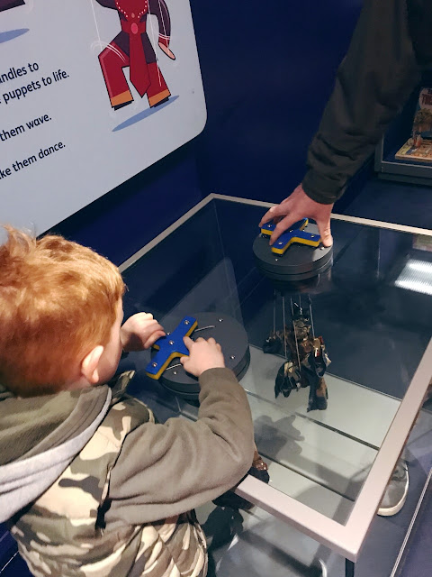 Father and son playing with puppets whilst in a display case