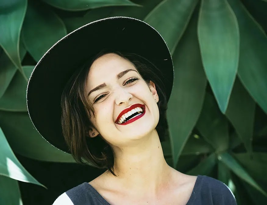 mujer-sonriendo-delante-de-plantas-verdes-con-sombrero