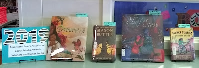Countertop display of books with sign: '2019 American Library Association / Youth Media Awards / Winners and Honor Books.' The books, arranged with front-covers facing forward, are, left to right: 'Dreamers' by Yuyi Morales, 'The Truth According to Mason Buttle' by Leslie Connor, 'The Stufff of Stars' by Marion Dane Bauer, and 'Merci Suarez Changes Gears' by Meg Medina.