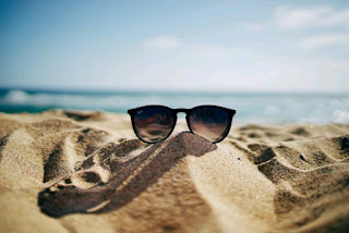 Black sunglasses on the sand with the sea in the background