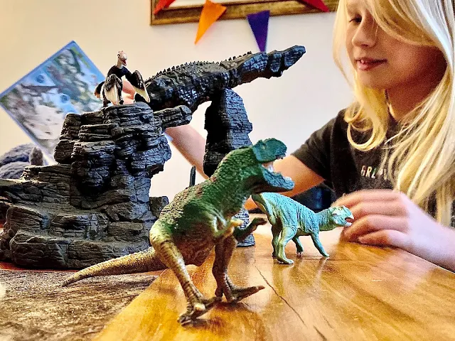 A girl playing with the Schleich Dinosaur sets to review them. The cave is set up as a catapult