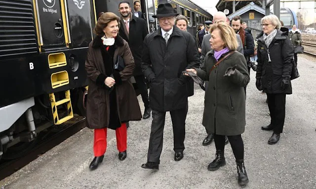 Queen Silvia wore a red poncho and red blazer pant suit. Gold leaf brooch and gold necklace. Governor Beatrice Ask