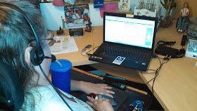 laurie wearign a headset and using Dragon Dictate at her desk with her computer and knick knacks around including a barbie doll in a wheelchair