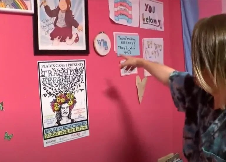 The child shows news reporters clippings about “you’re making history” and pride festivals on her bedroom wall.