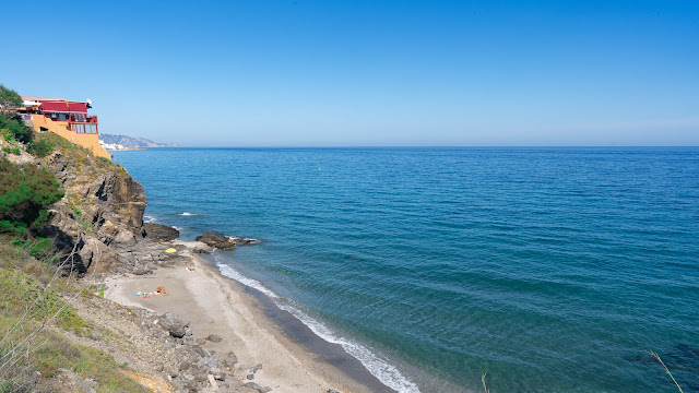 Playa con barrancos a su espalda con una construcción en lo alto, y el mar a su frente.