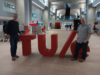 Stuart Murray and Ray Holt stand in front of large red letters T, U and e, representing the University of Eindhoven,