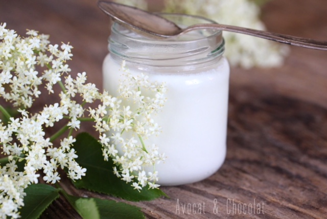 alt="yaourt blanc à la fleur de sureau sur une planche en bois décoré de fleur de sureau"