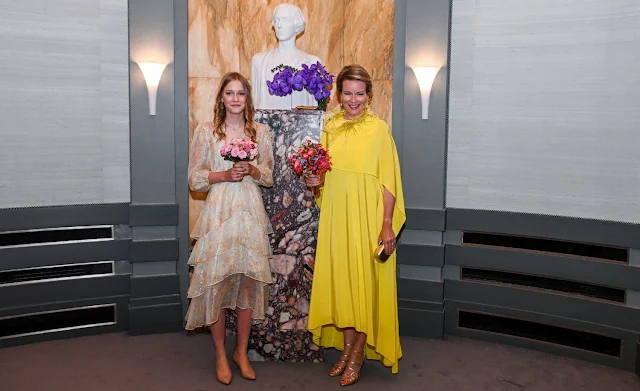 Princess Eleonore wore a Shiny floral print fluid silk dress by Maje. Queen Mathilde wore a yellow cape gown by Natan