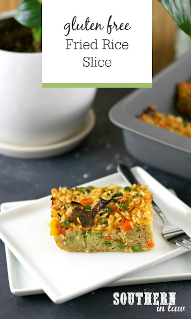 Easy Gluten Free Fried Rice Slice Recipe - slice of baked fried rice on white rectangular plate in front of grey baking dish and plant in white pot with peace lily