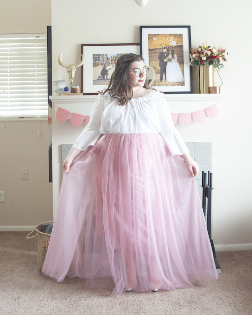 An outfit consisting of an off the shoulder white ruffle and bell sleeve blouse tucked into a pink tulle maxi skirt and nude heels.