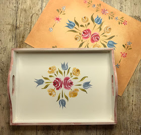 A photo of the completed Bauernmalerai pattern featuring red and yellow roses and blue tulips on a plain white tray next to the pattern/design sheet
