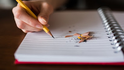 Writing with yellow pencil on a white notepad.