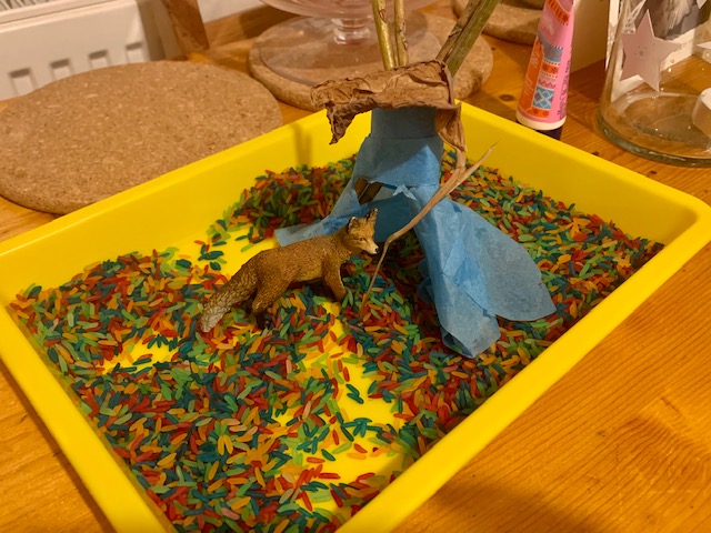 Rainbow rice in a tray, with stick tepee and toy fox