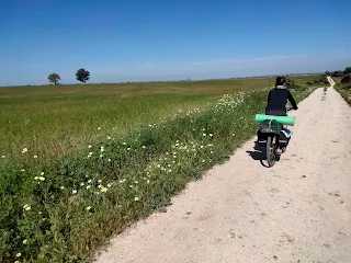 Aim'jie rides on a dirt road, flat landscape.