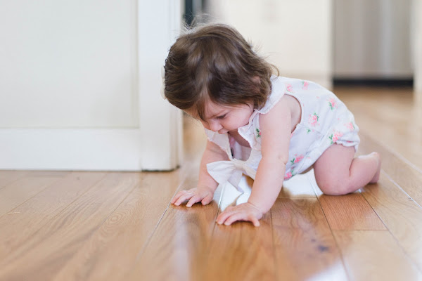 baby dressed in white with flowers crawling on hard wood floor